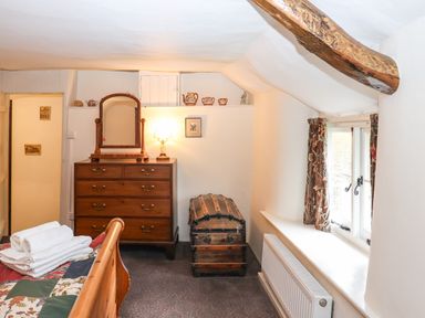 A bedroom with a wooden chest of drawers mirror and trunk near a window with curtains at Bridge Cottage in Dalwood
