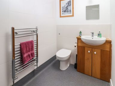 A bathroom with a toilet, a wooden vanity with a sink, soap bottles, a towel on a metal rack, and a framed picture on the wall at Bridge Cottage in Dalwood