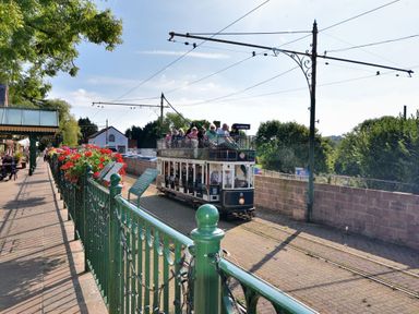 A tram with passengers on tracks next to a green metal fence with flowers and a platform at Bridge Cottage in Dalwood