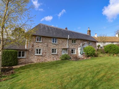 A stone cottage with a slate roof surrounded by a grass lawn and trees at Bridge Cottage in Dalwood
