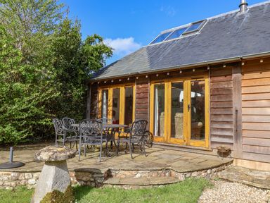 A patio with metal chairs and a table outside a wooden house with glass doors at Bridge Cottage in Dalwood