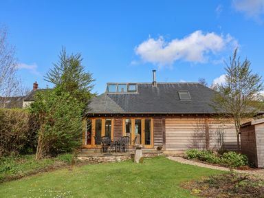 A backyard with green lawn and patio furniture in front of a wooden house at Bridge Cottage in Dalwood