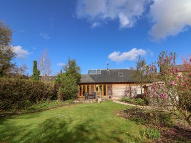 A garden with green grass trees and a wooden house with glass doors and a patio set at Bridge Cottage in Dalwood
