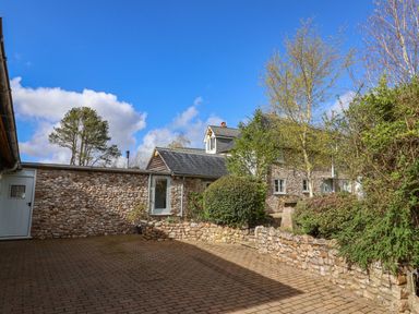 A stone house with a paved courtyard and various trees and bushes at Bridge Cottage in Dalwood