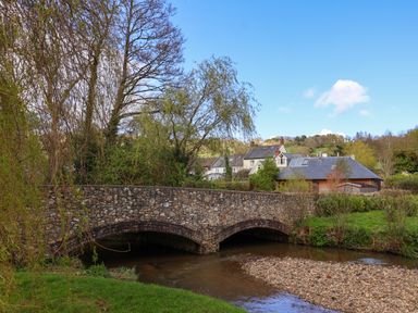 A stone bridge over a river with houses and trees in the background at Bridge Cottage in Dalwood