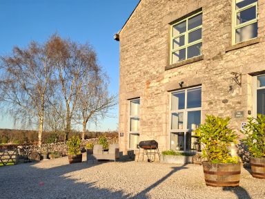 A stone building with large windows chairs potted plants and a barbecue outside at The Dairy at Brackenthwaite Farm Arnside