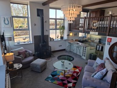 A living area with armchairs a sofa a fireplace and a kitchen with a breakfast bar at The Dairy at Brackenthwaite Farm in Arnside