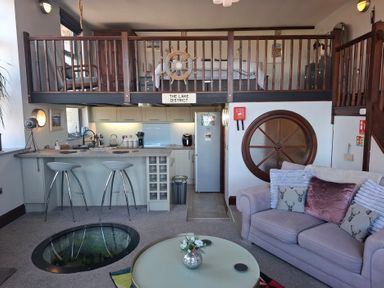 A living room and kitchen area with a loft bedroom above and a round glass floor window at The Dairy at Brackenthwaite Farm in Arnside