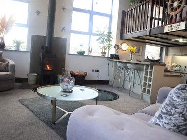 A living room with a wood stove near windows a round coffee table and bar stools at The Dairy at Brackenthwaite Farm in Arnside