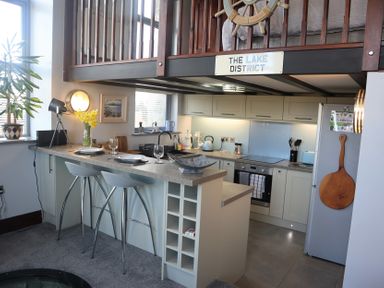 A kitchen with a breakfast bar stool and kitchen appliances under a loft at The Dairy at Brackenthwaite Farm in Arnside