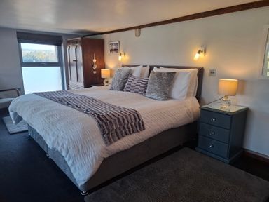 A bedroom with a large bed, bedside tables with lamps, a wooden wardrobe, and a window at The Dairy at Brackenthwaite Farm in Arnside