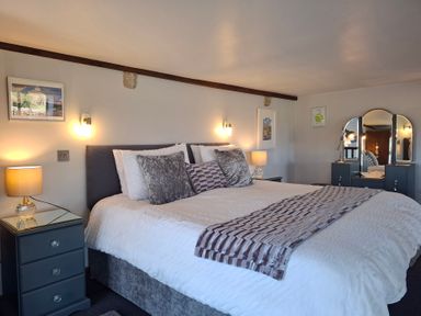 A bedroom with a large bed with white bedding and gray pillows two bedside tables with lamps and a vanity with a triple mirror at The Dairy at Brackenthwaite Farm in Arnside