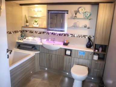 A bathroom with a bathtub towels sink toilet shelves and cabinets at The Dairy at Brackenthwaite Farm in Arnside