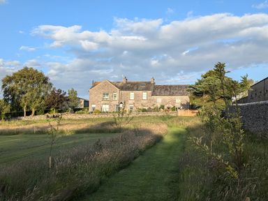A stone house at the end of a grassy path with trees and a stone wall at The Dairy at Brackenthwaite Farm in Arnside