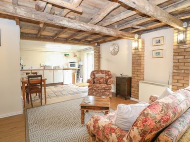 A living room with floral armchairs a wooden coffee table a dining table and a kitchenette with appliances at Pear Tree Barn in Stalham
