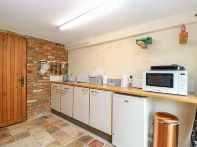 A kitchen with a wooden door brick wall cabinets microwave fridge and trash bin at Pear Tree Barn in Stalham