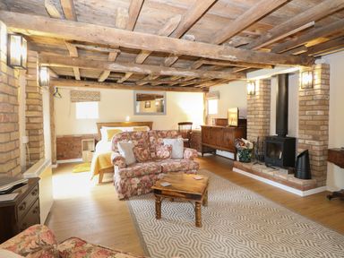 A living area with a floral sofa wooden coffee table bed wood burning stove and wooden beams on the ceiling at Pear Tree Barn in Stalham