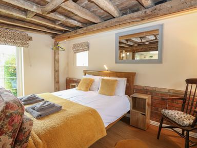 A bedroom with a wooden bed with yellow pillows and a yellow blanket at Pear Tree Barn in Stalham