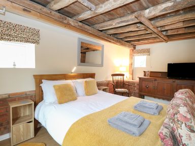 A bedroom with a wooden bed and yellow pillows and blanket a floral sofa a wooden cabinet with a television and a wooden chair at Pear Tree Barn in Stalham