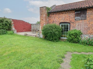 A brick house with a tiled roof and green bushes in front with a grassy yard and a stone path at Pear Tree Barn in Stalham