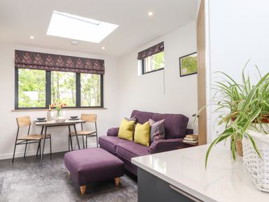 A small dining table with two chairs near windows and a purple sofa with cushions in a living area at Yew Tree Cabin in Ullswater