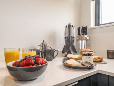 A kitchen counter with a bowl of strawberries and blueberries glasses of orange juice bread with jam and kitchen utensils at Yew Tree Cabin in Ullswater