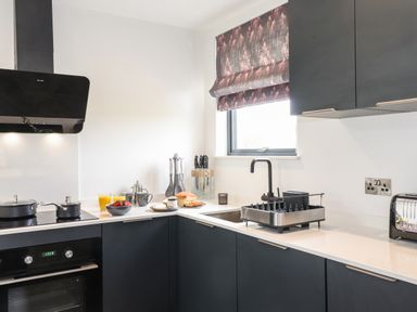A kitchen with black cabinets a black oven and stovetop a window with patterned blind and kitchen utensils on the counter at Yew Tree Cabin Ullswater