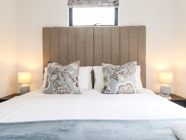 A bedroom with a bed made up with white linens blue floral pillows and matching lamps on bedside tables at Yew Tree Cabin in Ullswater
