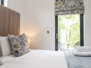A bedroom with a bed pillows and folded towels by a window with a view of a balcony and trees at Yew Tree Cabin Ullswater