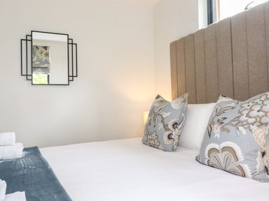 A bedroom with a bed with patterned pillows and a rectangular mirror on the wall at Yew Tree Cabin in Ullswater