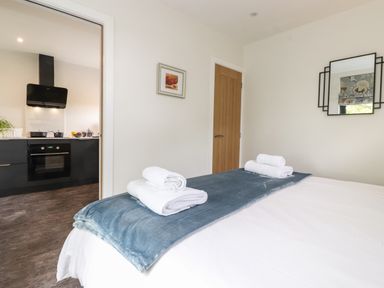 A bedroom with bed towels and a blue throw at the foot of the bed and a view of a kitchen through an open door at Yew Tree Cabin in Ullswater