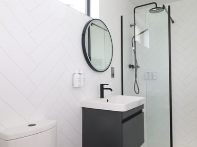A bathroom with a toilet sink with black faucet round mirror and walk in shower at Yew Tree Cabin in Ullswater