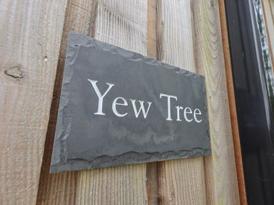 A wooden wall with a dark stone sign that says Yew Tree at Yew Tree Cabin Ullswater