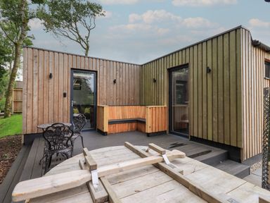 An outdoor deck area with wooden walls a wooden bench metal table and chairs at Yew Tree Cabin in Ullswater