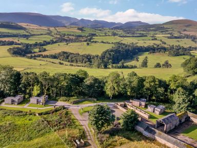 A rural landscape with wooden cabins trees and hills in the background at Yew Tree Cabin in Ullswater