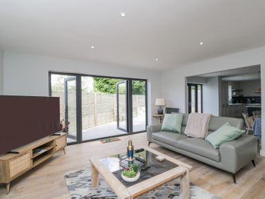 A living room with a grey sofa, a wooden coffee table, a wooden TV stand, and large glass doors opening to a patio at Greystones in Upton St Leonards