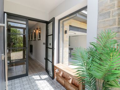 A hallway with patterned floor tiles and glass doors with black frames and a wooden bench with baskets and a green plant at Greystones in Upton St Leonards