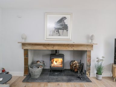 A fireplace with a wood-burning stove firewood baskets and a framed piano picture at Greystones in Upton St Leonards