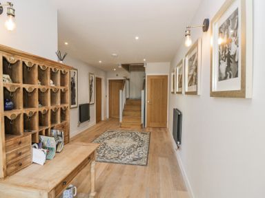 A hallway with wooden floor a wooden desk with cubbyholes a patterned rug stairs and framed pictures on the wall at Greystones in Upton St Leonards