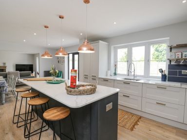 A kitchen with an island and bar stools with windows above the sink at Greystones in Upton St Leonards