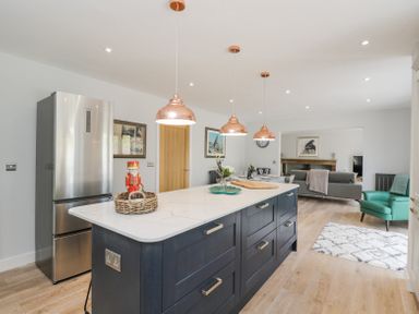 A kitchen with an island counter with copper pendant lights and a stainless steel refrigerator at Greystones in Upton St Leonards