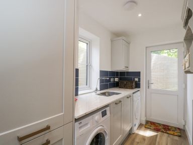 A utility room with a washing machine, sink, cabinets, and a door with a window at Greystones in Upton St Leonards