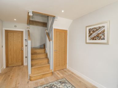 A hallway with wooden stairs and two wooden doors with a framed abstract painting on the wall at Greystones in Upton St Leonards