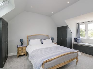 A bedroom with a bed bedside tables wardrobes and a window seat at Greystones in Upton St Leonards