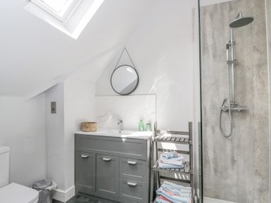 A bathroom with a gray vanity unit a round mirror a wooden towel rack with folded towels and a shower with a handheld and rain shower head at Greystones in Upton St Leonards