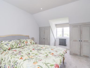 A bedroom with a bed with floral bedding two wardrobes and a window at Greystones in Upton St Leonards
