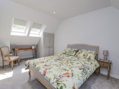 A bedroom with a bed with floral bedding a wooden chair a wooden desk under skylight windows and a wooden bedside table with a lamp at Greystones in Upton St Leonards