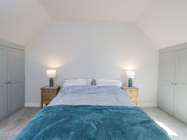 A bedroom with a bed between two bedside tables with lamps and built in wardrobes at Greystones in Upton St Leonards