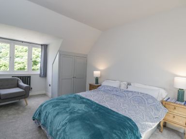 A bedroom with a double bed two bedside tables with lamps a grey armchair and a window at Greystones in Upton St Leonards