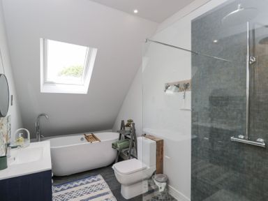 A bathroom with a bathtub under a skylight window a toilet a walk in shower and a sink at Greystones in Upton St Leonards